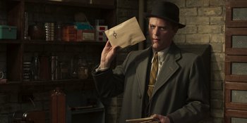 Movie still from “The Outfit” (2022), directed by Graham Moore – A man in a suit and hat holding a letter; Medium shot, Low angle