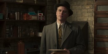 Movie still from “The Outfit” (2022), directed by Graham Moore – A man in a suit and hat holding a stack of papers; Medium shot, Low angle