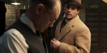 Movie still from “The Outfit” (2022), directed by Graham Moore – A man in a suit and a hat looking at another man in a suit and a hat; Medium shot, Over the shoulder angle