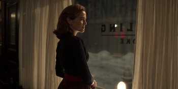 Movie still from “The Outfit” (2022), directed by Graham Moore – A woman standing in front of a window at night; Medium shot, Over the shoulder angle