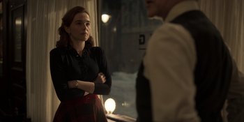 Movie still from “The Outfit” (2022), directed by Graham Moore – A man and a woman standing next to each other in front of a window at night; Medium shot, Over the shoulder angle