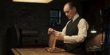 Movie still from “The Outfit” (2022), directed by Graham Moore – A man in a vest and tie is working on something; Medium shot, Low angle