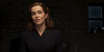 Movie still from “The Outfit” (2022), directed by Graham Moore – A woman in a black dress is standing in front of a brick wall; Close Up shot, Over the shoulder angle
