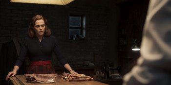 Movie still from “The Outfit” (2022), directed by Graham Moore – A woman in black shirt and red plaid skirt holding papers; Medium shot, Low angle