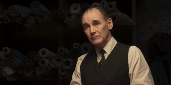 Movie still from “The Outfit” (2022), directed by Graham Moore – A man in a vest and tie standing in front of a bunch of rolls; Close Up shot, Low angle