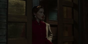 Movie still from “The Outfit” (2022), directed by Graham Moore – A woman in a red coat standing next to a man in a brown suit; Medium shot, Over the shoulder angle