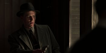 Movie still from “The Outfit” (2022), directed by Graham Moore – A man in a suit and hat holding a gun; Medium shot, Low angle