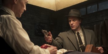 Movie still from “The Outfit” (2022), directed by Graham Moore – A man in a suit and hat holding a gun in his hand; Medium shot, Over the shoulder angle