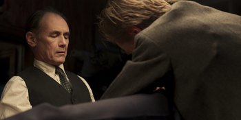 Movie still from “The Outfit” (2022), directed by Graham Moore – A man in a suit and tie looking at another man in a suit and tie; Medium shot, Over the shoulder angle