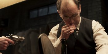 Movie still from “The Outfit” (2022), directed by Graham Moore – An older man sitting at a table with a bottle of wine; Close Up shot, Over the shoulder angle