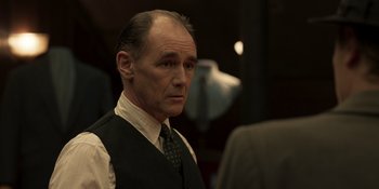 Movie still from “The Outfit” (2022), directed by Graham Moore – An older man wearing a vest and a tie; Close Up shot, Over the shoulder angle