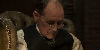 Movie still from “The Outfit” (2022), directed by Graham Moore – An older man wearing glasses and a tie; Close Up shot, High angle