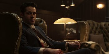 Movie still from “The Outfit” (2022), directed by Graham Moore – A man in a suit sitting in a chair in front of a lamp; Medium shot, Low angle