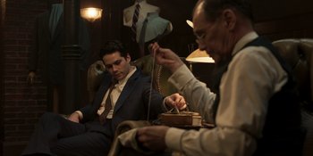 Movie still from “The Outfit” (2022), directed by Graham Moore – Two men in suits and ties sitting in a room; Medium shot, Over the shoulder angle