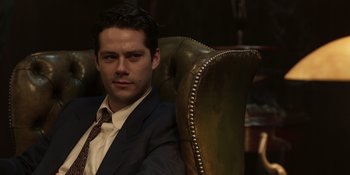 Movie still from “The Outfit” (2022), directed by Graham Moore – A man in a suit and tie sitting in a chair; Close Up shot, Low angle