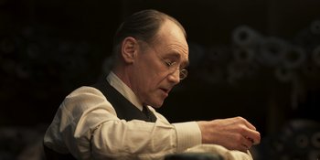 Movie still from “The Outfit” (2022), directed by Graham Moore – An older man wearing glasses and a white shirt; Close Up shot, Low angle