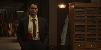 Movie still from “The Outfit” (2022), directed by Graham Moore – A man in a suit and tie standing in front of a mirror; Medium shot, Over the shoulder angle