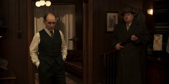 Movie still from “The Outfit” (2022), directed by Graham Moore – Two men standing in a living room next to each other; Medium shot, Over the shoulder angle