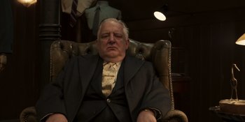 Movie still from “The Outfit” (2022), directed by Graham Moore – An older man sitting in a chair in a suit; Medium shot, Low angle