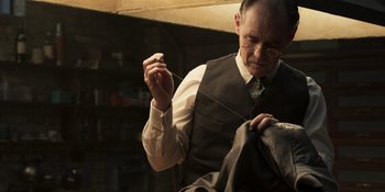 Movie still from “The Outfit” (2022), directed by Graham Moore – An old man in a vest and tie sewing a suit jacket; Medium shot, Over the shoulder angle