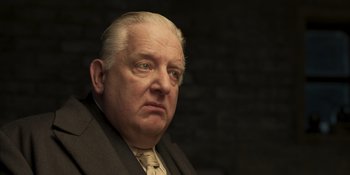 Movie still from “The Outfit” (2022), directed by Graham Moore – An older man in a suit and tie looking at the camera; Close Up shot, Low angle