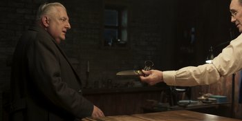 Movie still from “The Outfit” (2022), directed by Graham Moore – A man is handing a knife to another man in a suit; Medium shot, Over the shoulder angle