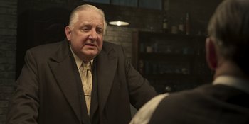 Movie still from “The Outfit” (2022), directed by Graham Moore – An older man wearing a suit and tie; Medium shot, Over the shoulder angle