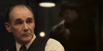 Movie still from “The Outfit” (2022), directed by Graham Moore – An older man wearing a vest and a tie; Close Up shot, Over the shoulder angle