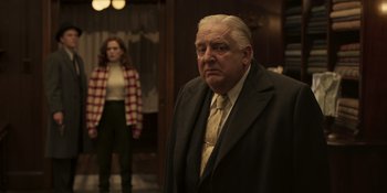Movie still from “The Outfit” (2022), directed by Graham Moore – An older man and a young woman standing in front of a door; Medium shot, Over the shoulder angle