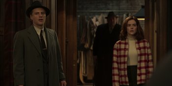 Movie still from “The Outfit” (2022), directed by Graham Moore – A man and a woman standing next to each other in a room; Medium shot, Over the shoulder angle