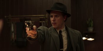 Movie still from “The Outfit” (2022), directed by Graham Moore – A man in a suit and hat is holding a gun; Medium shot, Over the shoulder angle