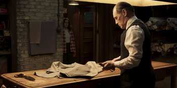 Movie still from “The Outfit” (2022), directed by Graham Moore – A man in a barber shop cutting a pair of scissors; Medium shot, Over the shoulder angle
