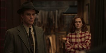 Movie still from “The Outfit” (2022), directed by Graham Moore – A man and a woman standing next to each other in a room; Medium shot, Over the shoulder angle