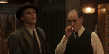 Movie still from “The Outfit” (2022), directed by Graham Moore – Two men in suits and ties smoking a cigarette; Medium shot, Low angle