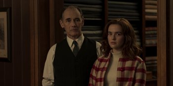 Movie still from “The Outfit” (2022), directed by Graham Moore – A man standing next to a woman in a room; Medium shot, Over the shoulder angle