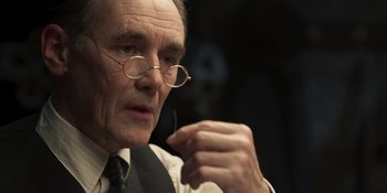 Movie still from “The Outfit” (2022), directed by Graham Moore – An older man wearing glasses and a tie; Close Up shot, Over the shoulder angle