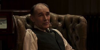 Movie still from “The Outfit” (2022), directed by Graham Moore – An older man sitting on a leather couch; Close Up shot, High angle