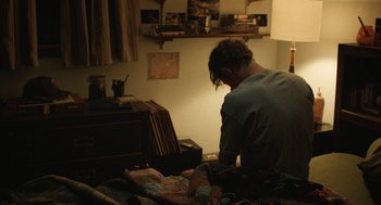 Movie still from “The Passenger” (2023), directed by Carter Smith – A man sitting on top of a bed in a room; Medium shot, High angle