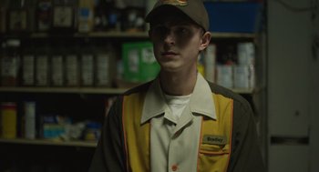 Movie still from “The Passenger” (2023), directed by Carter Smith – A young man in a baseball cap is wearing a uniform; Medium shot, Over the shoulder angle