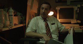 Movie still from “The Passenger” (2023), directed by Carter Smith – A man sitting in a chair in a room; Medium shot, Low angle