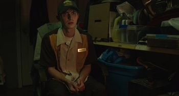 Movie still from “The Passenger” (2023), directed by Carter Smith – A man sitting on a chair in a room; Medium shot, High angle