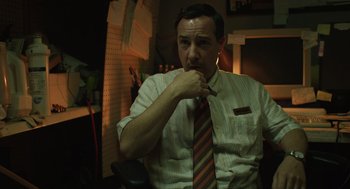 Movie still from “The Passenger” (2023), directed by Carter Smith – A man wearing a striped neck tie is smoking a cigarette; Medium shot, Low angle
