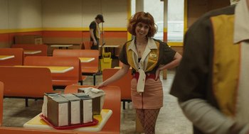 Movie still from “The Passenger” (2023), directed by Carter Smith – A woman dressed as an airline stewardess in an airport; Medium shot, Over the shoulder angle