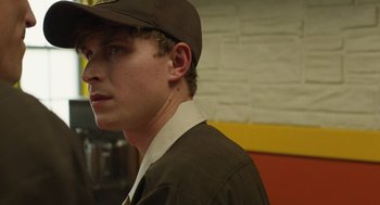 Movie still from “The Passenger” (2023), directed by Carter Smith – A young man wearing a brown hat and a brown jacket; Close Up shot, Over the shoulder angle