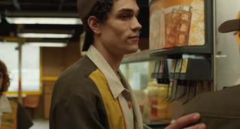 Movie still from “The Passenger” (2023), directed by Carter Smith – A young man in a hat is standing in front of a display case; Close Up shot, Low angle