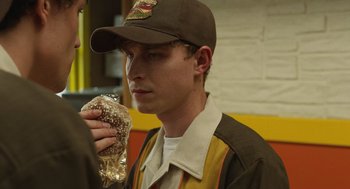 Movie still from “The Passenger” (2023), directed by Carter Smith – A man in a baseball cap holding a hot dog; Close Up shot, Over the shoulder angle