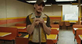 Movie still from “The Passenger” (2023), directed by Carter Smith – A man holding a tie in an empty restaurant; Medium shot, Low angle