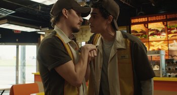 Movie still from “The Passenger” (2023), directed by Carter Smith – Two young men are holding hands in a restaurant; Medium shot, Low angle