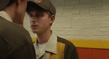 Movie still from “The Passenger” (2023), directed by Carter Smith – A young man wearing a brown hat and a brown jacket; Close Up shot, Over the shoulder angle