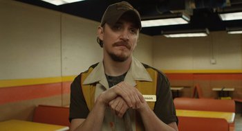 Movie still from “The Passenger” (2023), directed by Carter Smith – A man in a hat and a brown jacket is posing for a picture; Close Up shot, Low angle